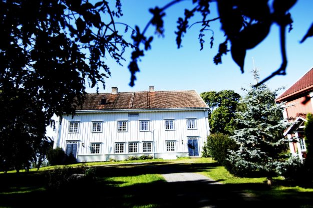 Storslått hvitmalt trebygning med hage i forgrunnen