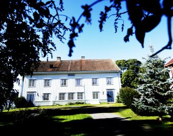 Storslått hvitmalt trebygning med hage i forgrunnen