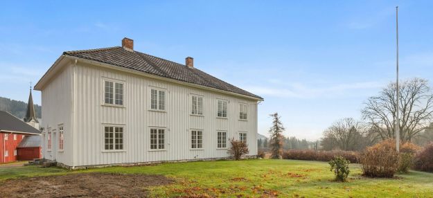 Stor hvit trebygning med hage og flaggstang i forgrunnen