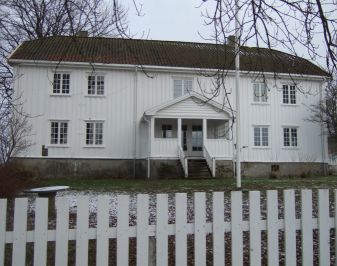 Hvitmalt hovedbygning med stakittgjerde i forgrunnen