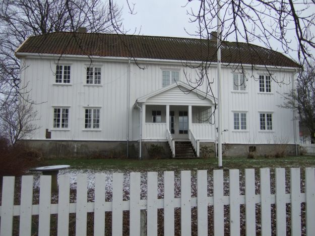 Hvitmalt hovedbygning med stakittgjerde i forgrunnen