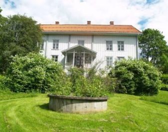 Hvitmalt hovedbygning med parkmessig hageanlegg rundt