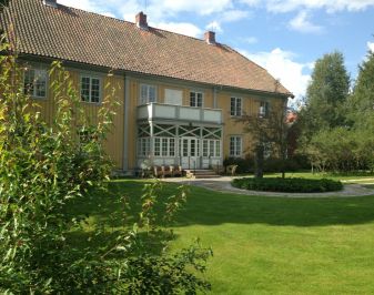 Gulmalt trebygning med parkmessig hage rundt