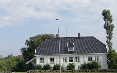 Hvitt trehus med hekk og flaggstang i forkant