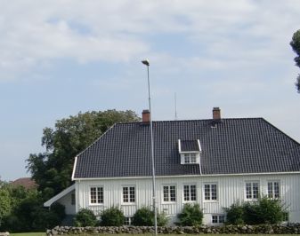 Hvitt trehus med hekk og flaggstang i forkant