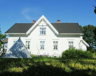 Hvitmalt hus med hage i forgrunnen