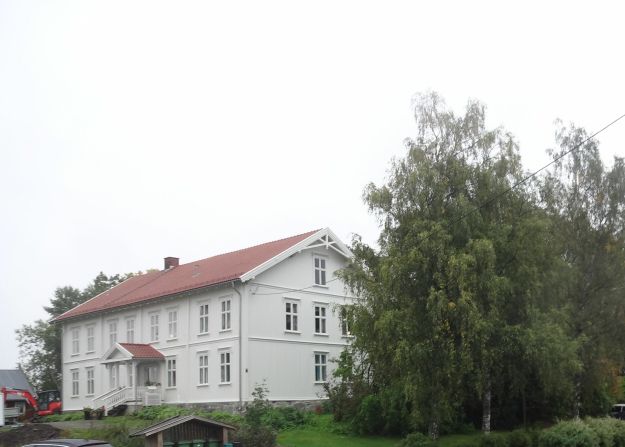 Hvitmalt tømmerbygning med litt av hagen foran