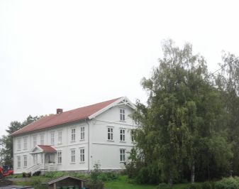 Hvitmalt tømmerbygning med litt av hagen foran