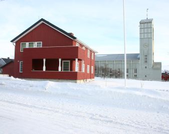 Rødt trehus fra etterkrigsårene kirke i bakgrunn snedekket.