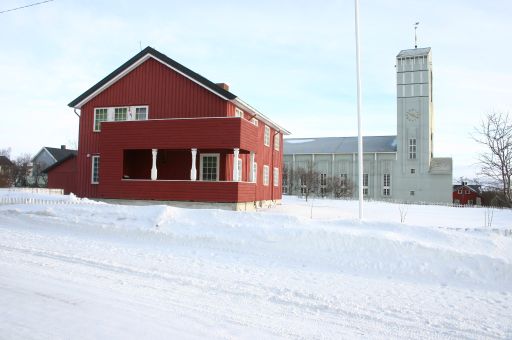 Rødt trehus fra etterkrigsårene kirke i bakgrunn snedekket.