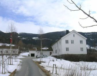 Gårdstun med stort hvitt våningshus. Vinterbilde