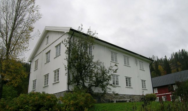 Stort, hvitt våningshus med rød låve i bakgrunnen