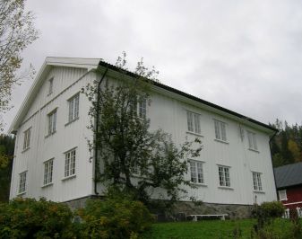 Stort, hvitt våningshus med rød låve i bakgrunnen