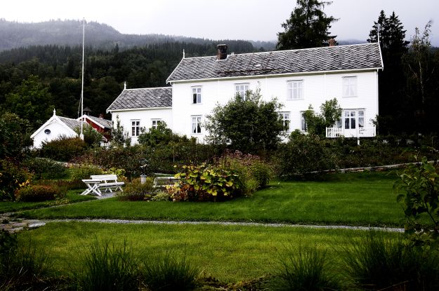 Meldal prestebolig. Hvitt trehus omgitt av grønn mark og blomsterbusker.