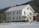 Åmli prestebolig. Hvitt trehus i snødekt landskap.