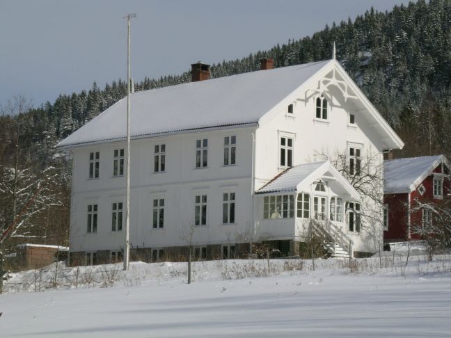 Åmli prestebolig. Hvitt trehus i snødekt landskap.