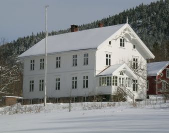 Åmli prestebolig. Hvitt trehus i snødekt landskap.