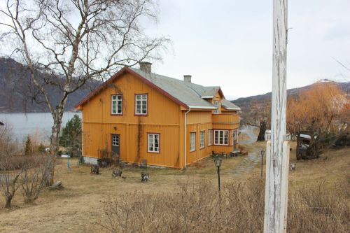 Gulmalt hus med hage og flaggstang i forkant