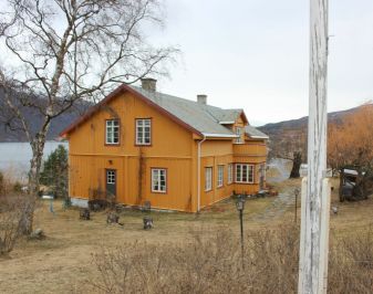 Gulmalt hus med hage og flaggstang i forkant