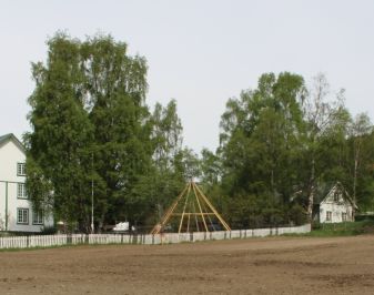 Hvitmalt hus i to etasjer, gårdstun med stakittgjerde og hage i bakkant.