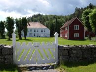 Holt prestegård. To trehus omgitt av skog og grønn mark. Foto