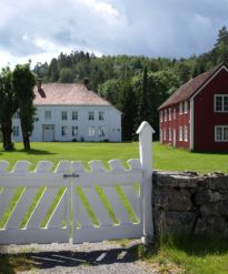 Holt prestegård. To trehus omgitt av skog og grønn mark. Foto