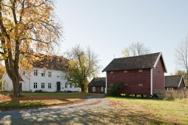 Hvitmalt våningshus med stabbur og innkjøring i forgrunnen