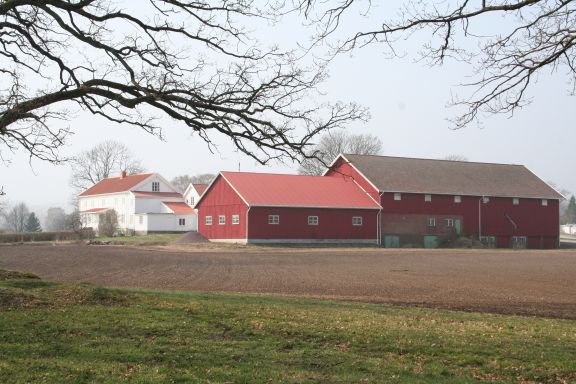 Stort gårdsbruk med jorder og låve i forgrunnen