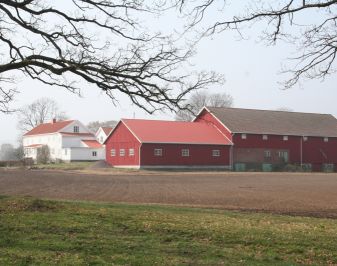 Stort gårdsbruk med jorder og låve i forgrunnen