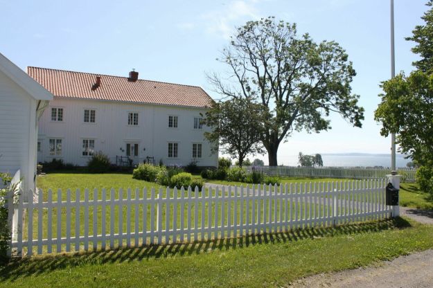 Hvitmalt stort hus med stakittgjerde og hage foran