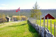Lesja prestegård omgitt av grønn mark med norgesflagg som vaier i vinden. Foto