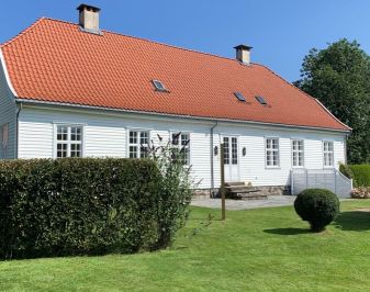 Hvitmalt hus med hage og hekk