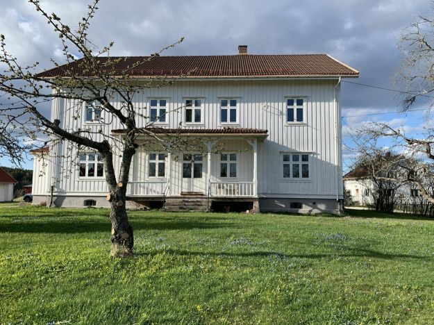 Hvitmalt stort hus med hage foran
