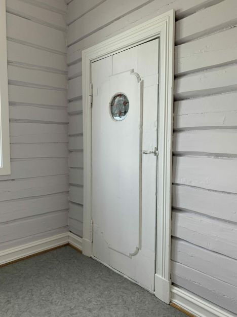 Hvitmalt innerdør med rundt speil og laftevegger