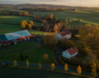 Ullensaker prestegård sett ovenfra. Tre bygninger omgitt av grønn mark. Foto