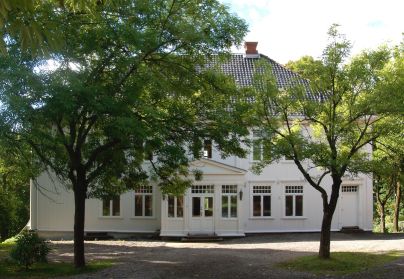 Stor toetasjes trehusbygning med store trær foran