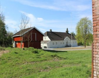 Hvitt trehus med rødmalt stabbur i forkant