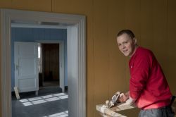 Mann i rød genser inne i hus med gule vegger.