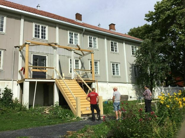 Fire menn foran foran trehus med nybygd trapp.